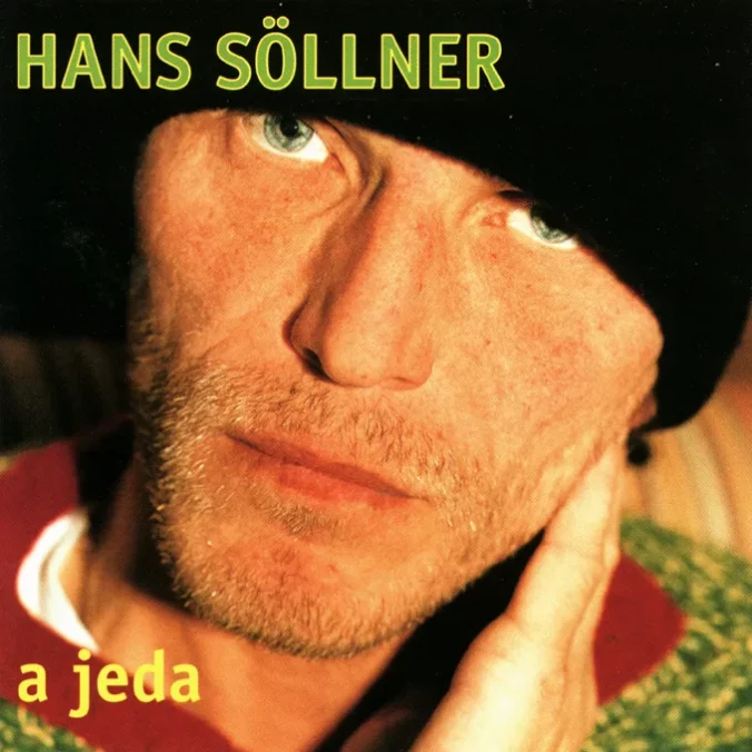 Hans SÖLLNER auf dem Coverbild ganz nah und in Farbe, seine blau-grünen Augen sehen in die Kamera, er trägt eine schwarze Mütze und ein rot-grünes Oberteil